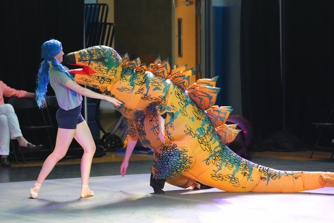 a dancer with blue hair dances with the dino figure